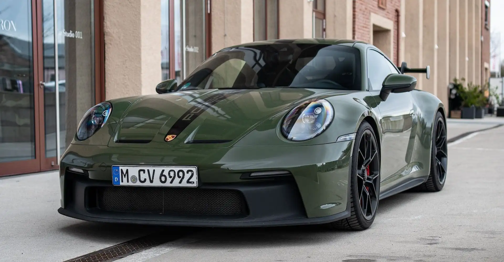 Our olive green Porsche GT3 photographed from the front in front of an industrial building. 